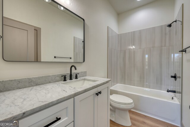 full bathroom with tiled shower / bath, vanity, wood-type flooring, and toilet