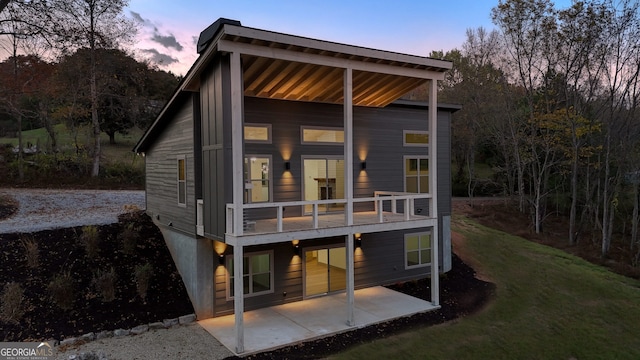 back house at dusk featuring a patio area and a lawn