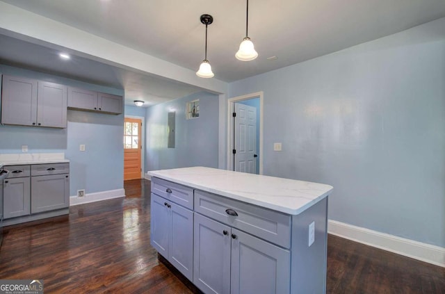 kitchen featuring gray cabinetry, a kitchen island, pendant lighting, dark wood-type flooring, and light stone counters