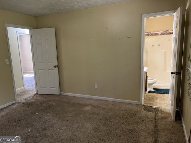 unfurnished bedroom featuring a spacious closet, light carpet, a textured ceiling, and ensuite bathroom