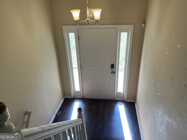 foyer with an inviting chandelier, a healthy amount of sunlight, and dark wood-type flooring