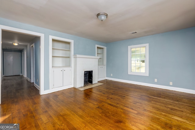 unfurnished living room featuring a brick fireplace, dark hardwood / wood-style floors, and built in shelves