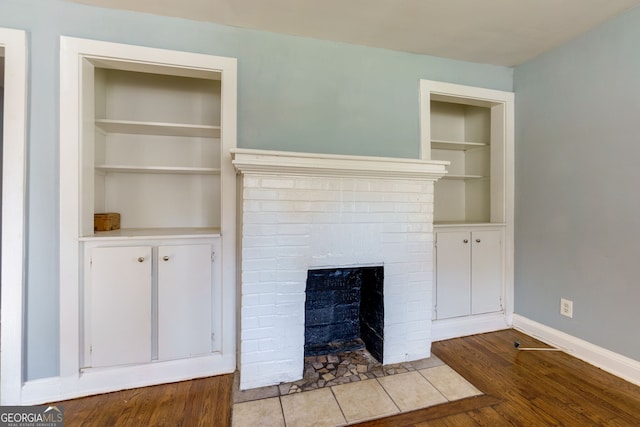 unfurnished living room featuring light hardwood / wood-style floors, built in features, and a brick fireplace