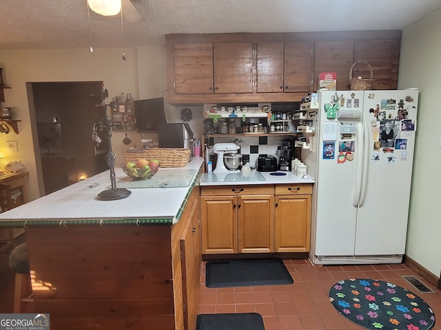 kitchen with ceiling fan, a textured ceiling, white refrigerator with ice dispenser, tile counters, and tile patterned floors