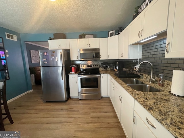 kitchen featuring appliances with stainless steel finishes, sink, backsplash, white cabinetry, and light hardwood / wood-style flooring