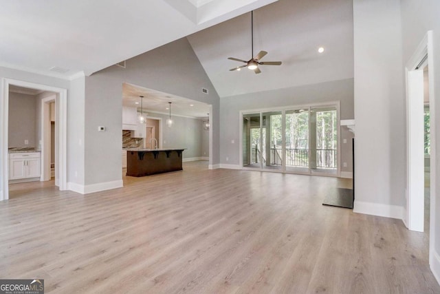 unfurnished living room featuring a high ceiling, ceiling fan, sink, and light hardwood / wood-style floors