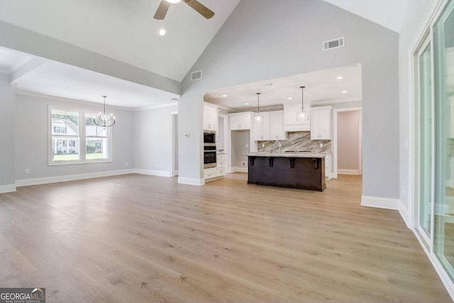 unfurnished living room featuring ceiling fan with notable chandelier, high vaulted ceiling, and light hardwood / wood-style flooring