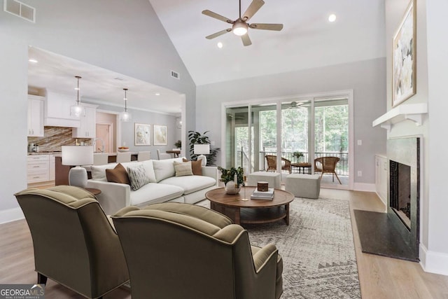 living room with sink, ceiling fan, high vaulted ceiling, a fireplace, and light hardwood / wood-style floors