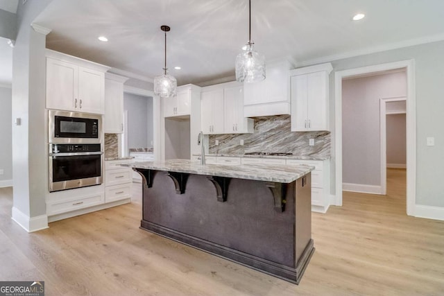 kitchen with white cabinetry, decorative light fixtures, a kitchen island with sink, and appliances with stainless steel finishes