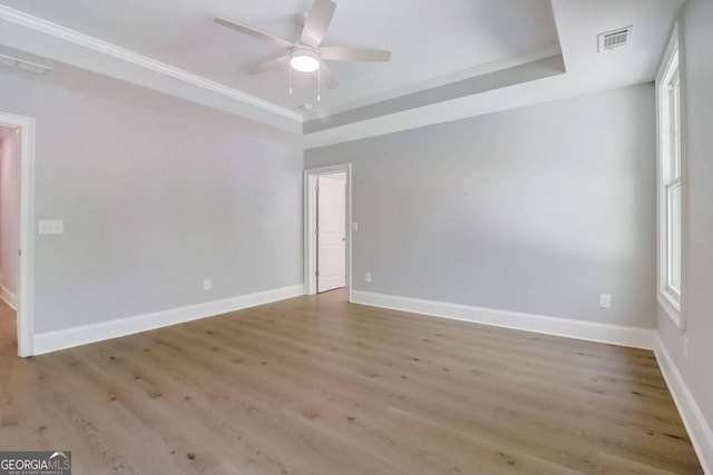 spare room with hardwood / wood-style flooring, crown molding, ceiling fan, and a tray ceiling