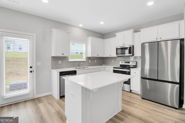 kitchen with sink, a center island, white cabinets, appliances with stainless steel finishes, and light hardwood / wood-style floors