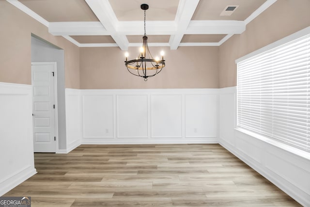 unfurnished dining area with coffered ceiling, beam ceiling, ornamental molding, a chandelier, and light hardwood / wood-style floors