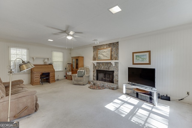 carpeted living room featuring a stone fireplace, crown molding, wood walls, and ceiling fan