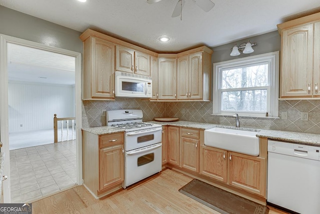 kitchen with light brown cabinets, light wood-style flooring, decorative backsplash, white appliances, and a sink