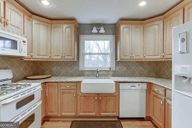 kitchen with light wood-style flooring, light stone counters, white appliances, backsplash, and a sink