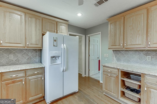 kitchen featuring visible vents, light brown cabinetry, light stone counters, and white refrigerator with ice dispenser