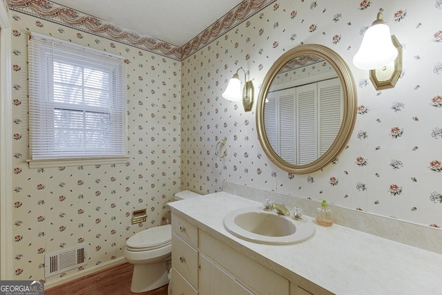 half bathroom featuring wallpapered walls, visible vents, vanity, and toilet