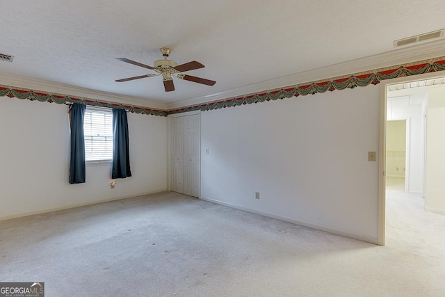 empty room featuring light colored carpet, visible vents, ornamental molding, a textured ceiling, and ceiling fan