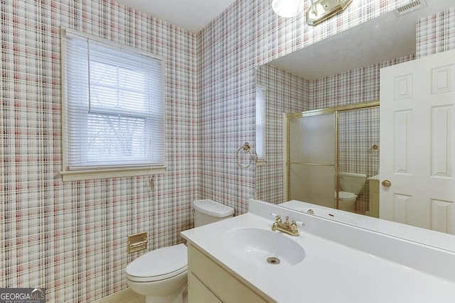 full bathroom with a shower with door, toilet, vanity, and visible vents