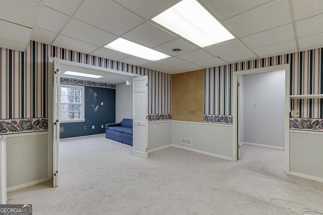 basement featuring wallpapered walls, a drop ceiling, light colored carpet, and visible vents