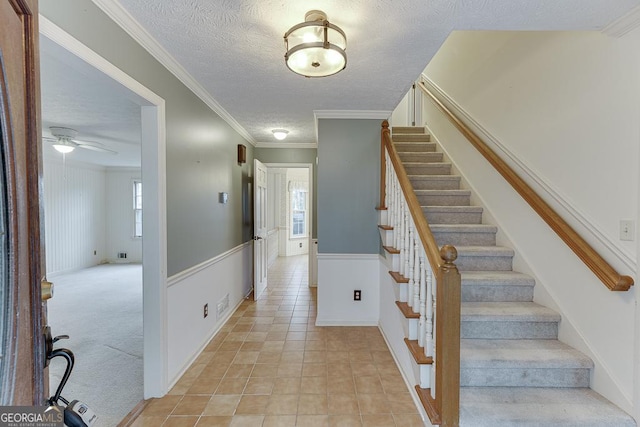 stairway with wainscoting, tile patterned floors, a ceiling fan, crown molding, and a textured ceiling