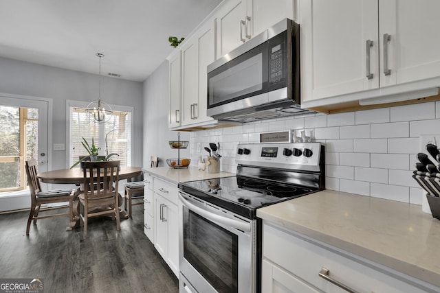 kitchen featuring appliances with stainless steel finishes, white cabinetry, pendant lighting, dark wood-type flooring, and light stone counters