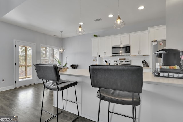 kitchen with appliances with stainless steel finishes, a kitchen bar, decorative light fixtures, and white cabinets