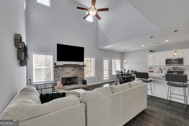 living room with ceiling fan, a healthy amount of sunlight, dark hardwood / wood-style floors, and a stone fireplace