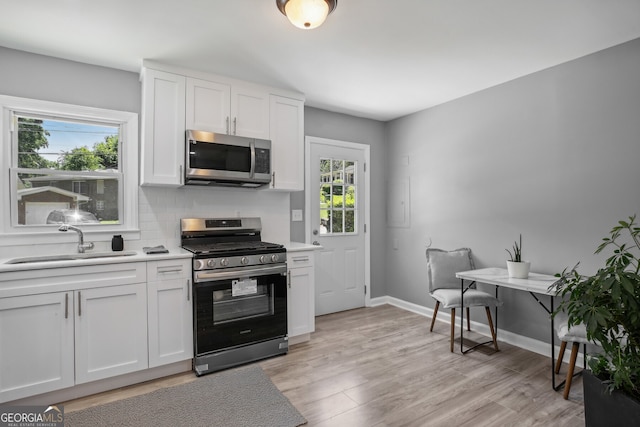 kitchen with sink, light hardwood / wood-style flooring, backsplash, stainless steel appliances, and white cabinets