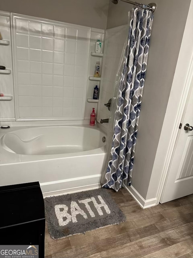 full bath featuring wood finished floors, shower / bath combo with shower curtain, and baseboards