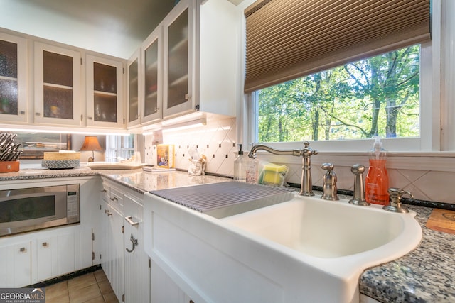 kitchen featuring white cabinetry, backsplash, stainless steel microwave, and sink