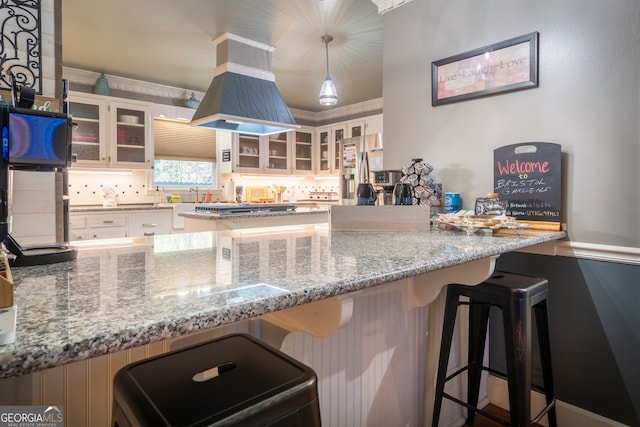 kitchen with island range hood, a kitchen breakfast bar, decorative light fixtures, white cabinets, and light stone counters