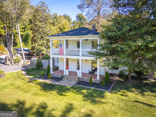 view of front facade with a balcony, a front yard, a patio area, and ceiling fan