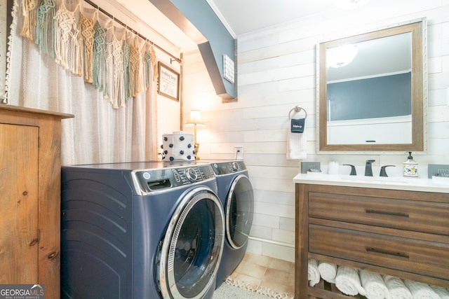 laundry room with light tile patterned floors, washing machine and clothes dryer, wood walls, crown molding, and sink