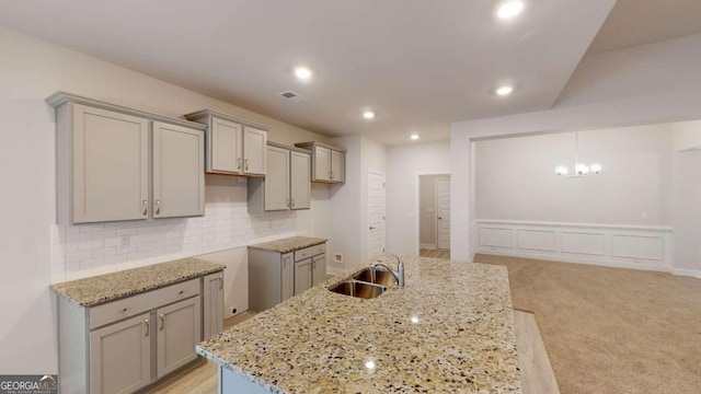 kitchen featuring backsplash, light stone countertops, sink, light colored carpet, and a center island