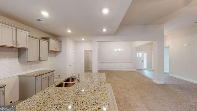 kitchen featuring light stone counters, decorative backsplash, sink, and light colored carpet