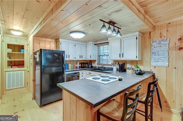 kitchen with kitchen peninsula, white cabinets, black appliances, and wooden walls