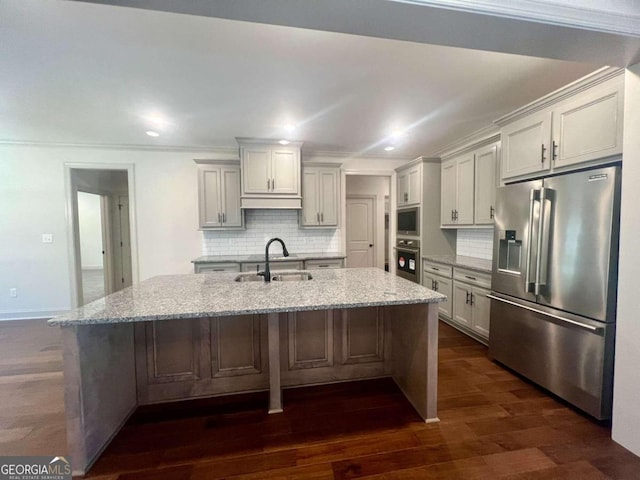 kitchen with backsplash, appliances with stainless steel finishes, an island with sink, light stone countertops, and sink