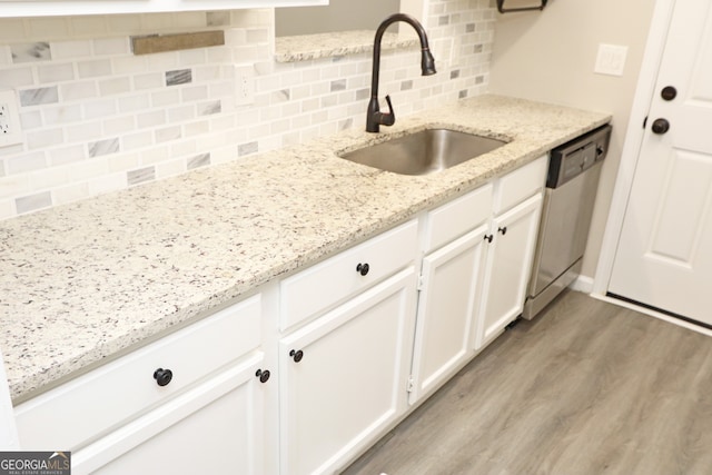 kitchen with sink, dishwasher, white cabinetry, light hardwood / wood-style floors, and light stone counters