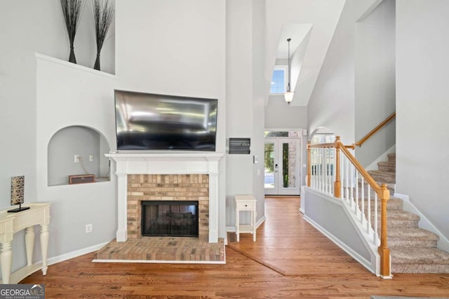 living room featuring a fireplace, hardwood / wood-style floors, french doors, and a high ceiling