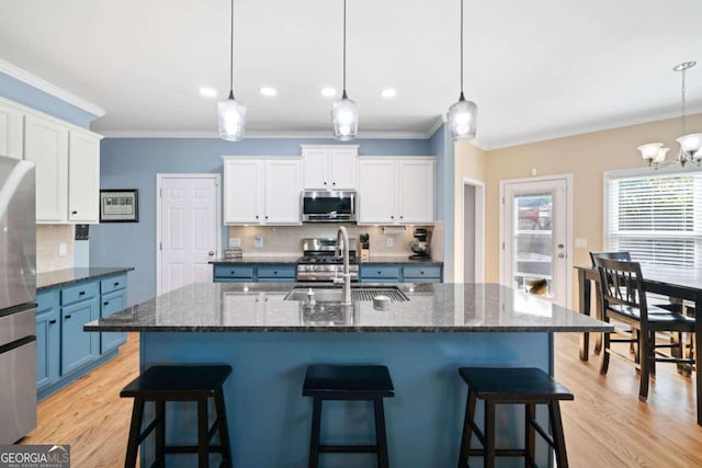 kitchen with blue cabinetry, appliances with stainless steel finishes, decorative light fixtures, and an island with sink