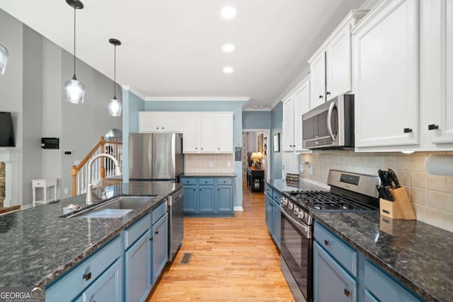 kitchen with appliances with stainless steel finishes, sink, blue cabinets, white cabinetry, and light hardwood / wood-style floors