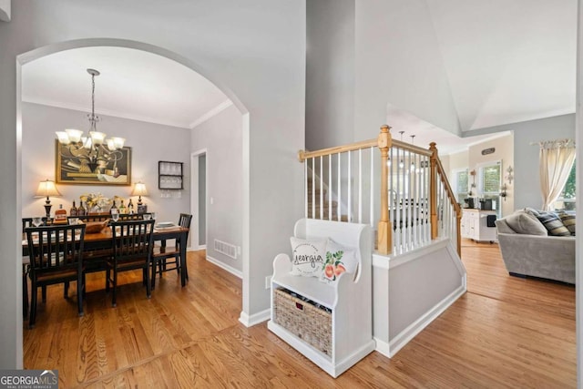 interior space with an inviting chandelier, light hardwood / wood-style flooring, vaulted ceiling, and crown molding