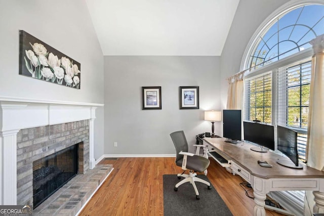 office with vaulted ceiling, a fireplace, and hardwood / wood-style flooring