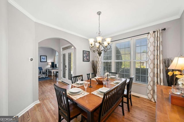 dining area with crown molding, a notable chandelier, and light hardwood / wood-style flooring