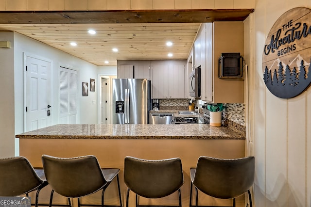 kitchen with dark stone countertops, backsplash, appliances with stainless steel finishes, and kitchen peninsula