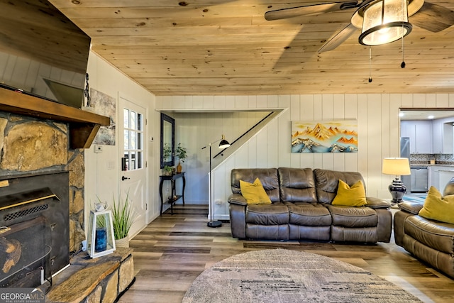 living room featuring hardwood / wood-style floors, wood ceiling, a stone fireplace, and wood walls