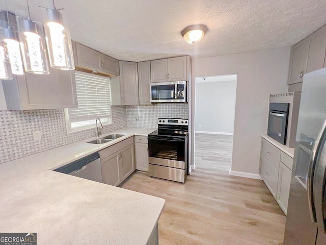 kitchen with light hardwood / wood-style flooring, stainless steel appliances, sink, pendant lighting, and tasteful backsplash