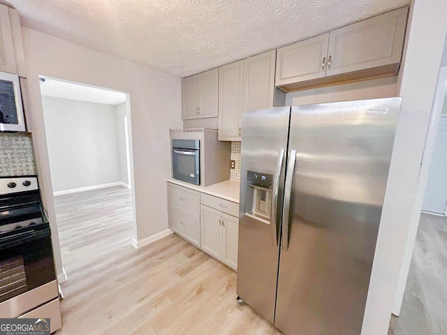 kitchen with backsplash, appliances with stainless steel finishes, a textured ceiling, and light hardwood / wood-style floors