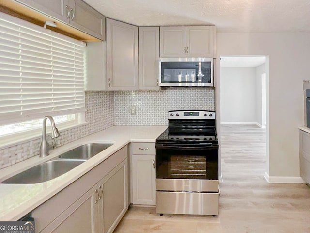 kitchen featuring tasteful backsplash, appliances with stainless steel finishes, a textured ceiling, light hardwood / wood-style floors, and sink